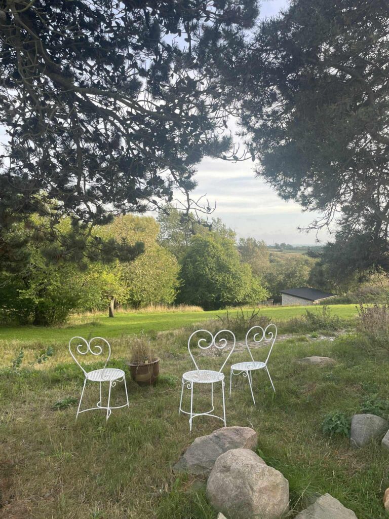 Garden with white chairs under large trees and a view over the landscape